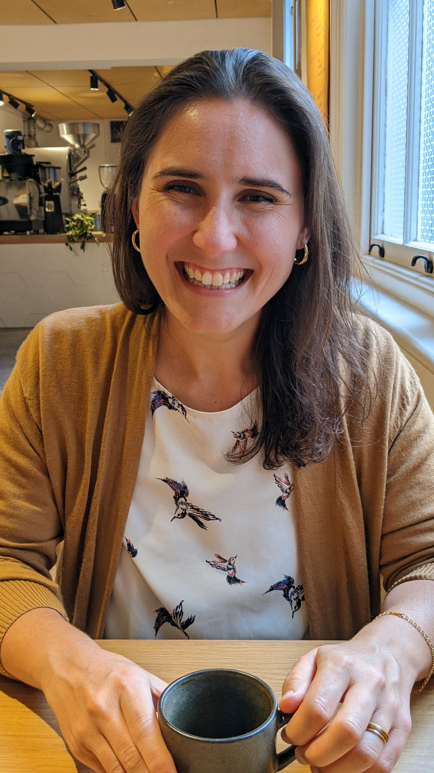 A picture of Steph smiling holding a coffee cup for a 'virtual coffee' meeting